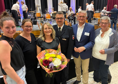 Die Organisator:innen stehen mit Blumenstrauß vor dem Orchester.