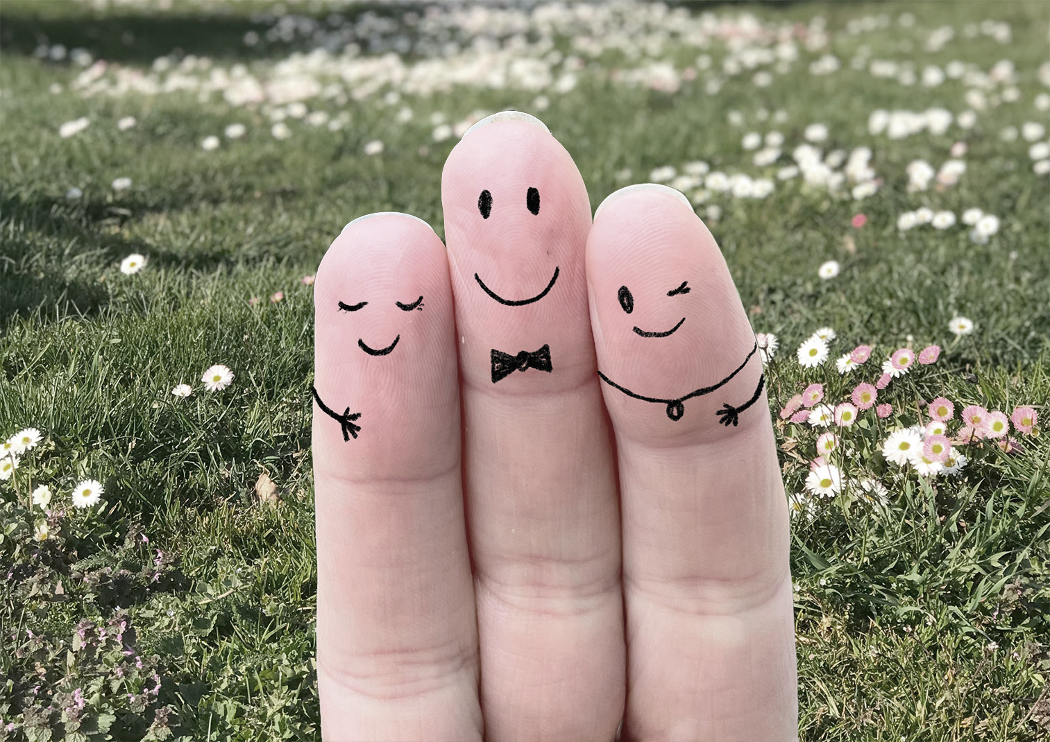 Drei Finger einer Hand, die mit Gesichtern bemalt sind.